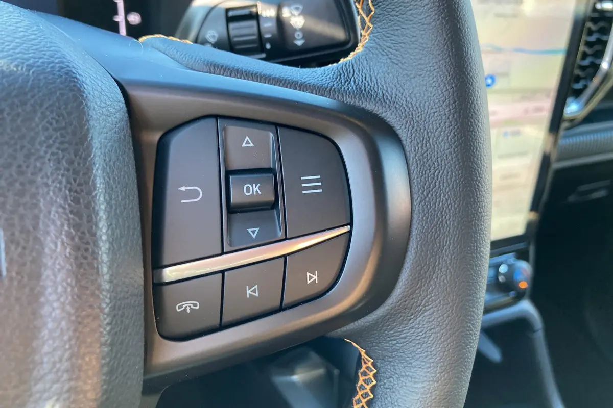 Gros plan sur les commandes au volant du Ford Ranger 2025 Wildtrak Plus, cuir noir avec surpiqûres orange visibles.