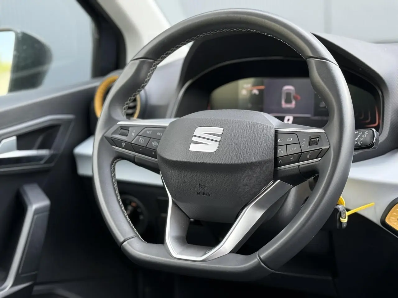 Vue rapprochée du volant multifonction noir de la SEAT Arona 2025 avec tableau de bord digital en arrière-plan.