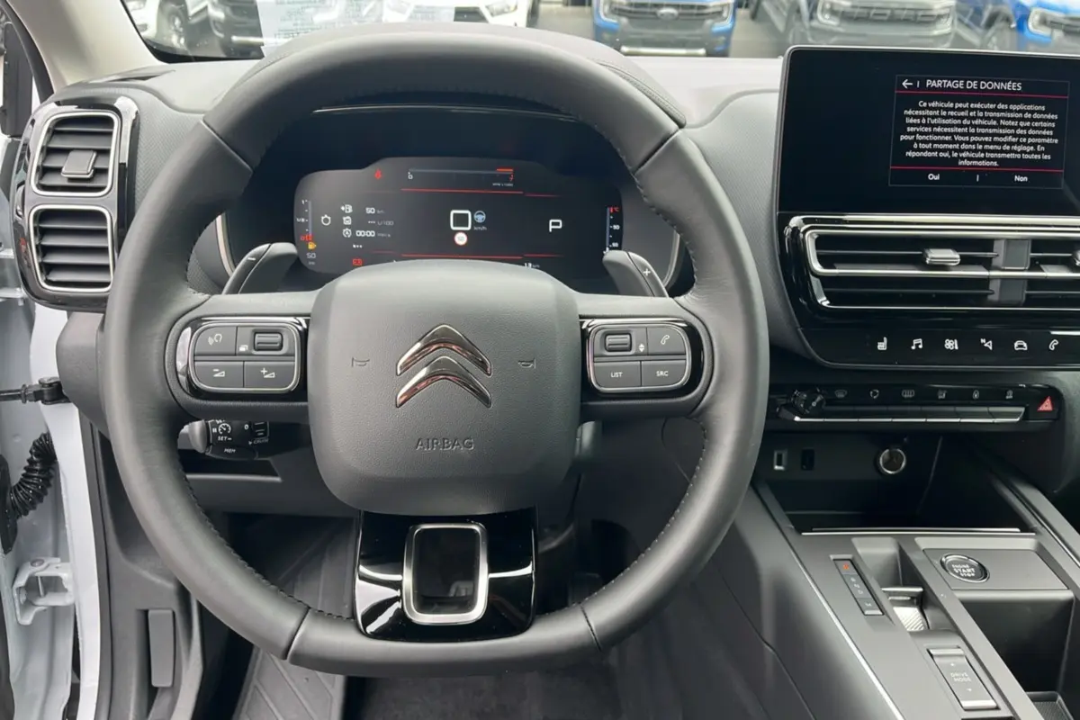 Vue intérieure centrée sur le volant cuir multifonctions et tableau de bord digital du Citroën C5 Aircross blanc okénite.