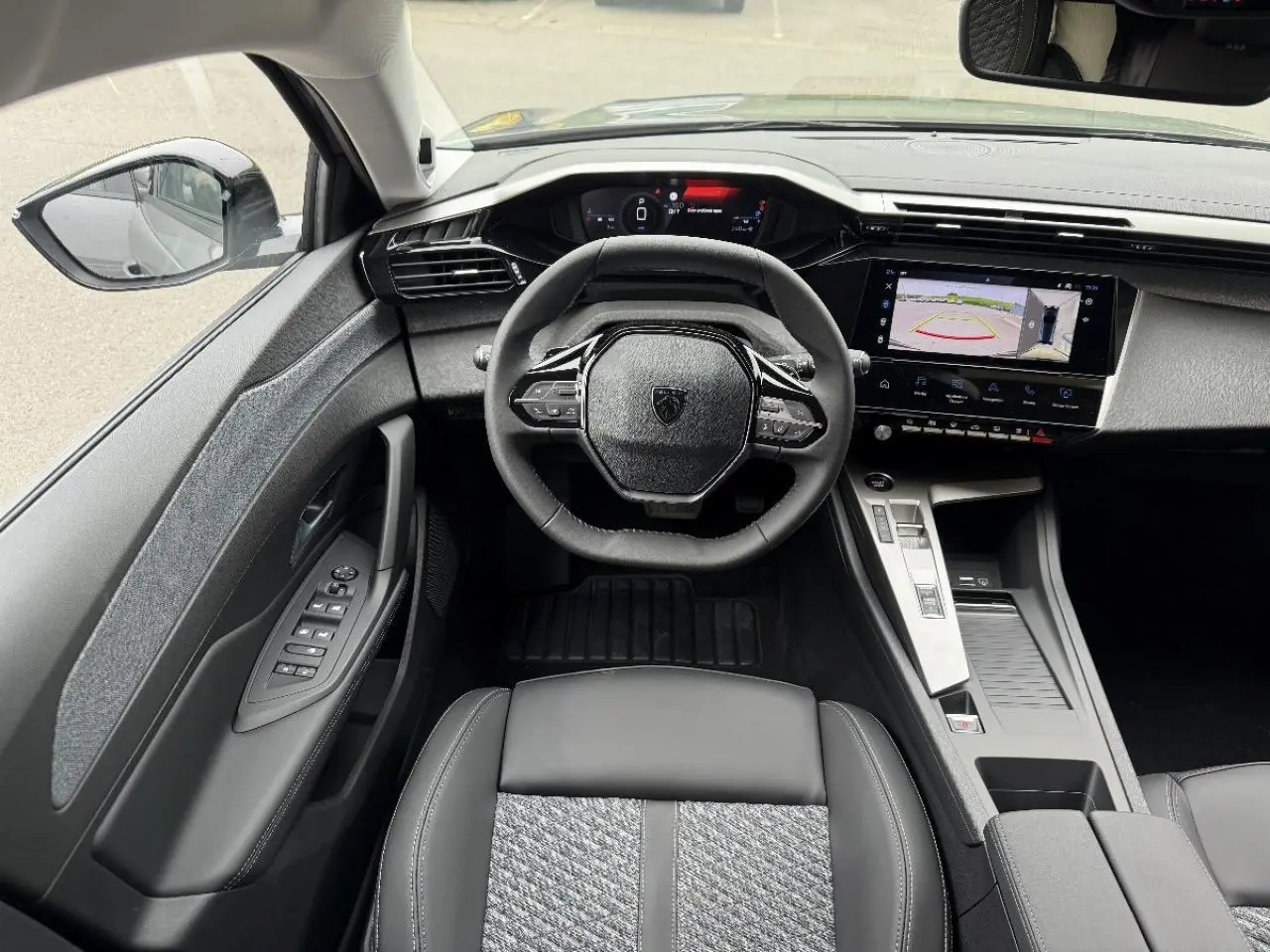 Vue intérieure de face du poste de conduite de la Peugeot 308 2026 gris sélénite avec écran tactile et volant compact.