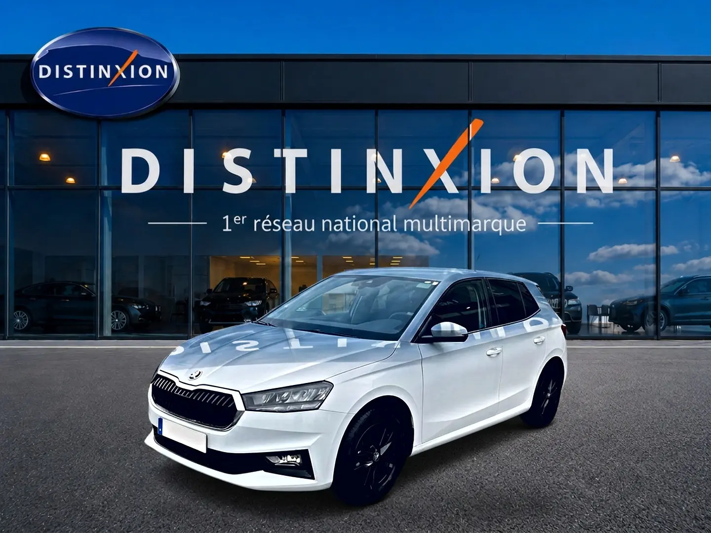 SKODA FABIA blanche vue 3/4 avant droit, jantes noires, devant vitrine Distinxion reflet ciel bleu.