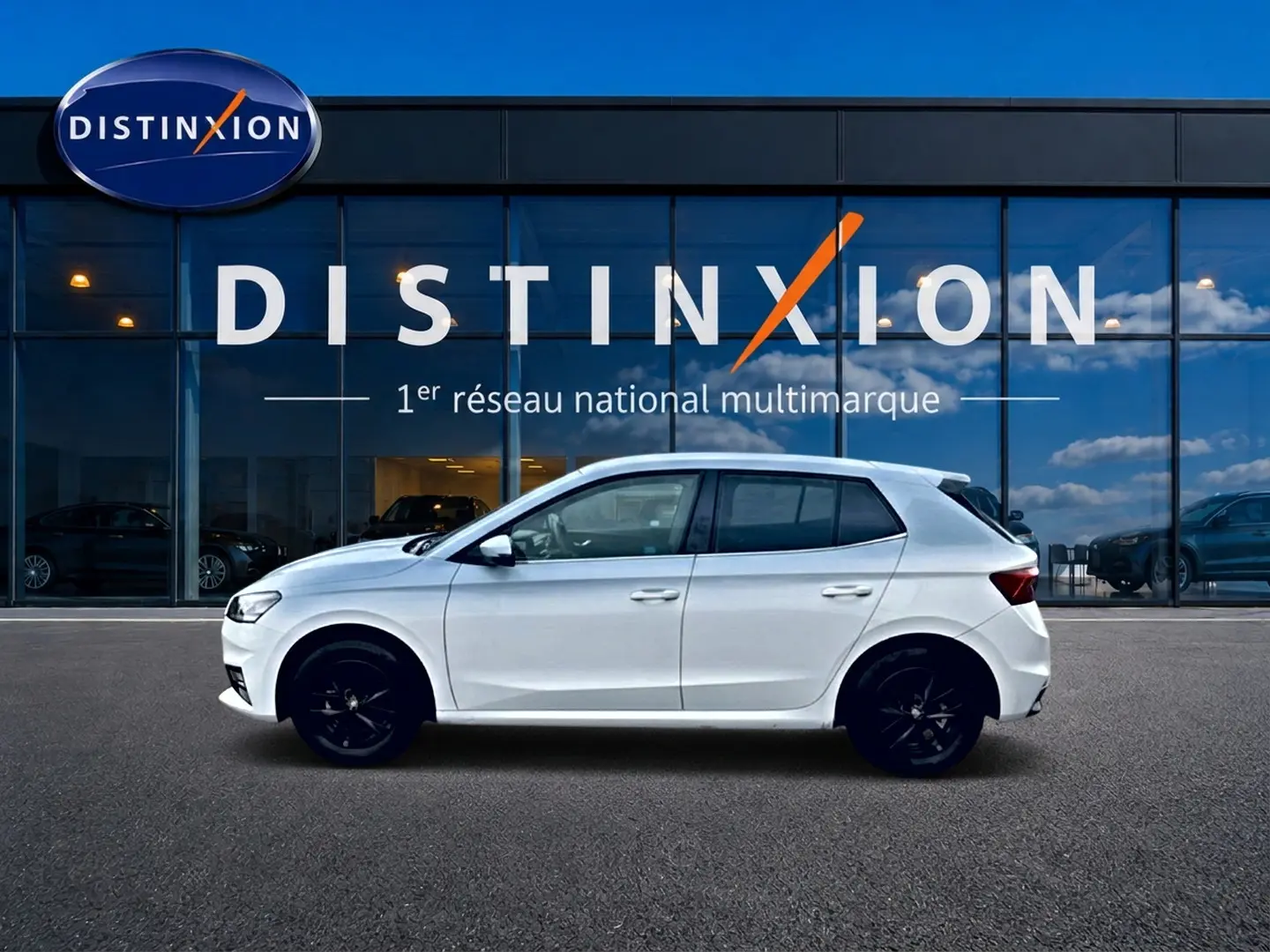 Profil droit d'une Skoda Fabia blanche 2025 avec jantes noires, garée devant une vitrine Distinxion.