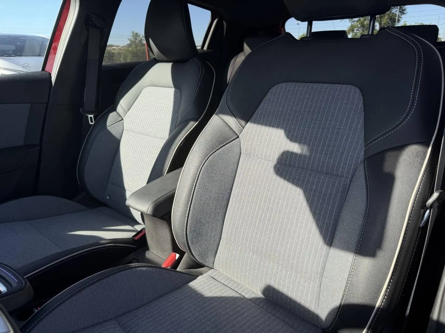 Vue intérieure des sièges avant gris clair et foncé de la Renault Clio 1.0 Eco-G 100ch Techno 2025, avec accoudoir central.