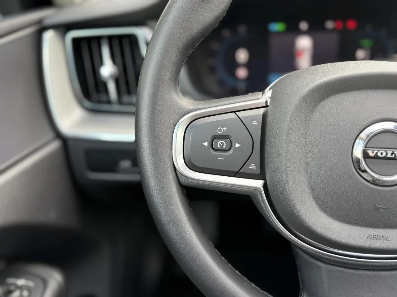Gros plan sur le volant simili-cuir gris du Volvo XC60 T6 AWD PHEV 2024, avec commandes de régulateur de vitesse.