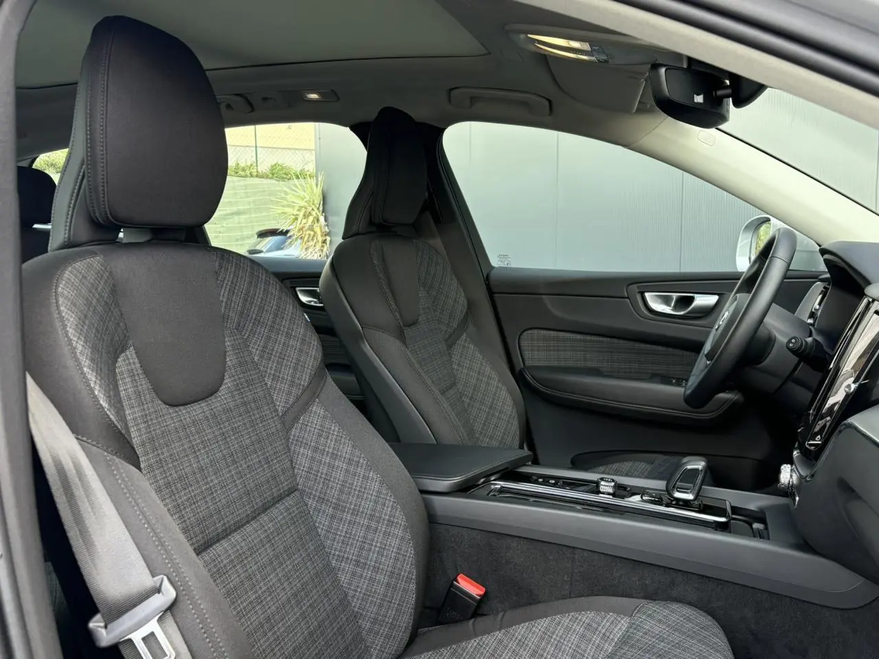 Vue intérieure côté conducteur du Volvo XC60 gris Silver 2024, sièges tissu à motif écossais et console centrale moderne.