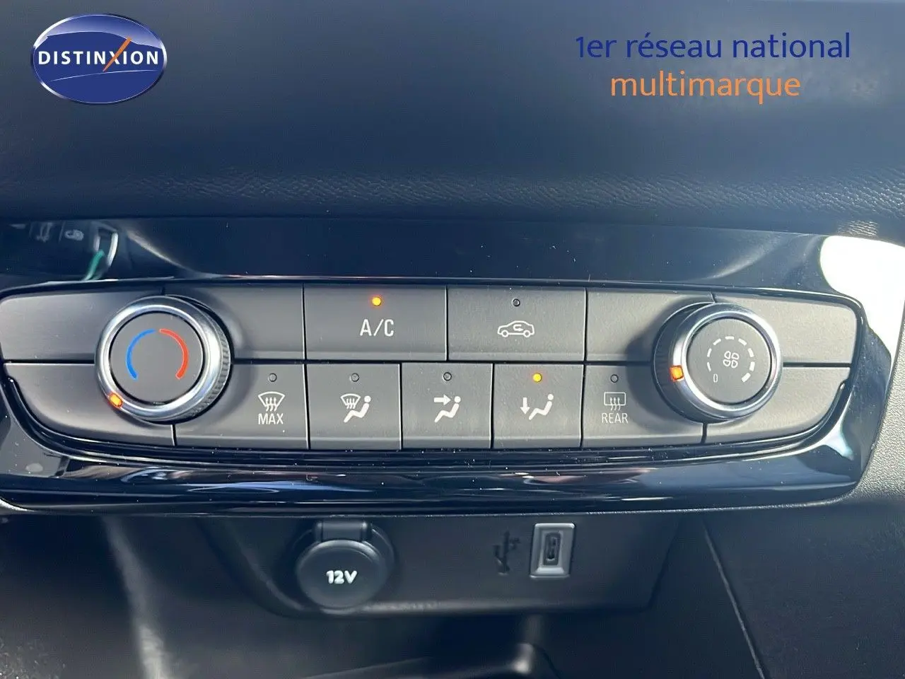 Gros plan sur la console de climatisation de l'Opel Corsa gris Kristal Metal, avec commandes et prise 12V visibles.