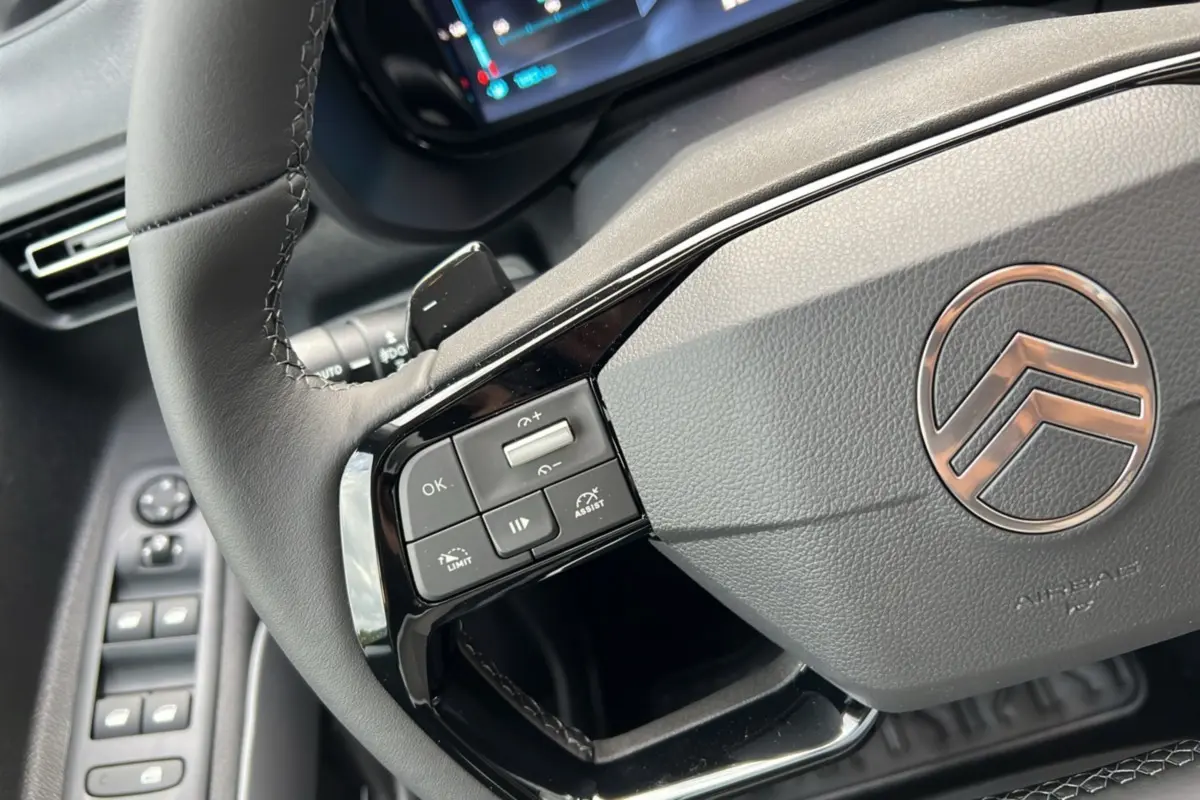 Gros plan sur le volant cuir du Citroën Berlingo 2025 avec commandes intégrées et logo chrome au centre.