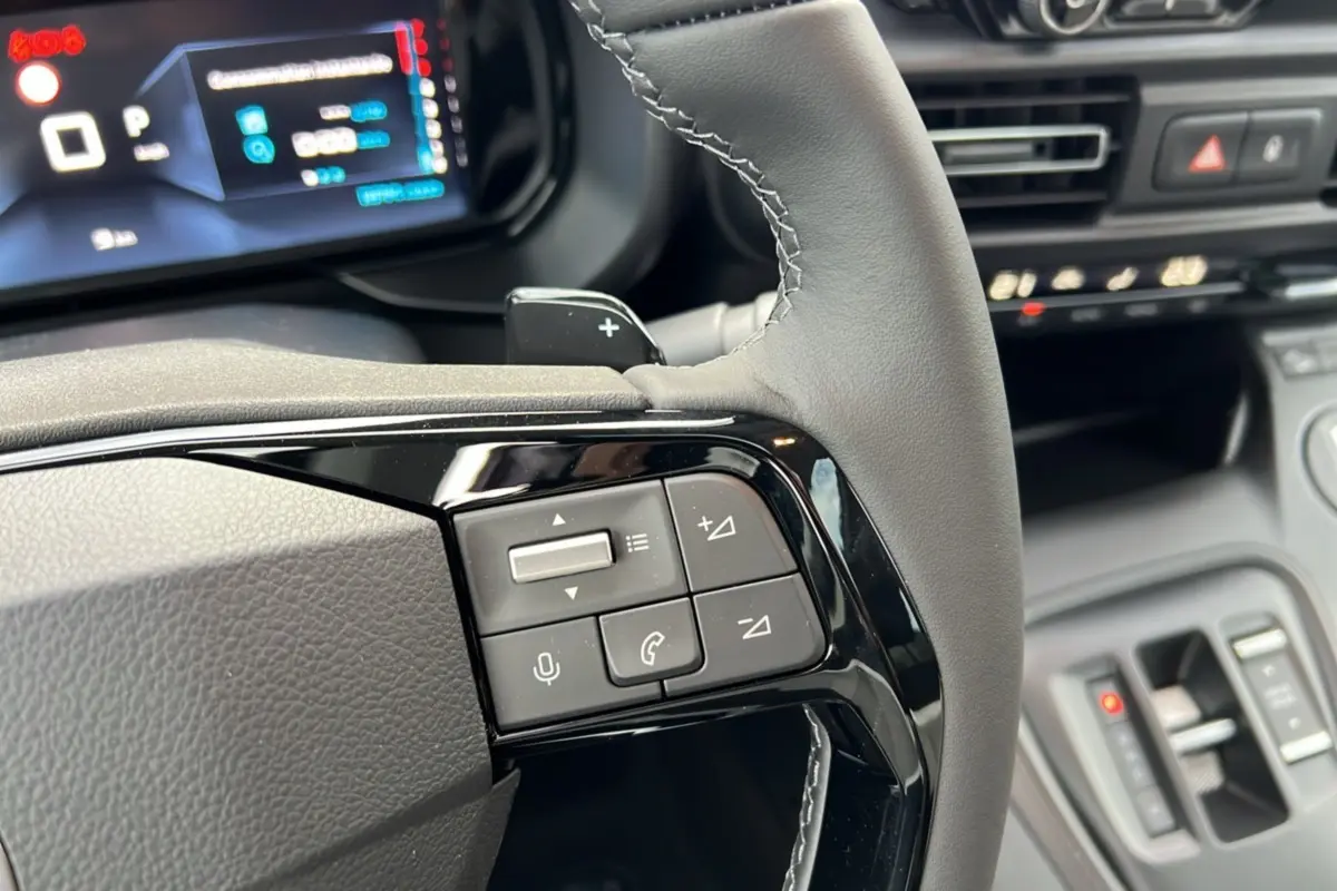 Gros plan sur les commandes au volant du Citroën Berlingo 2025 noir perla nera, avec tableau de bord numérique en arrière-plan.