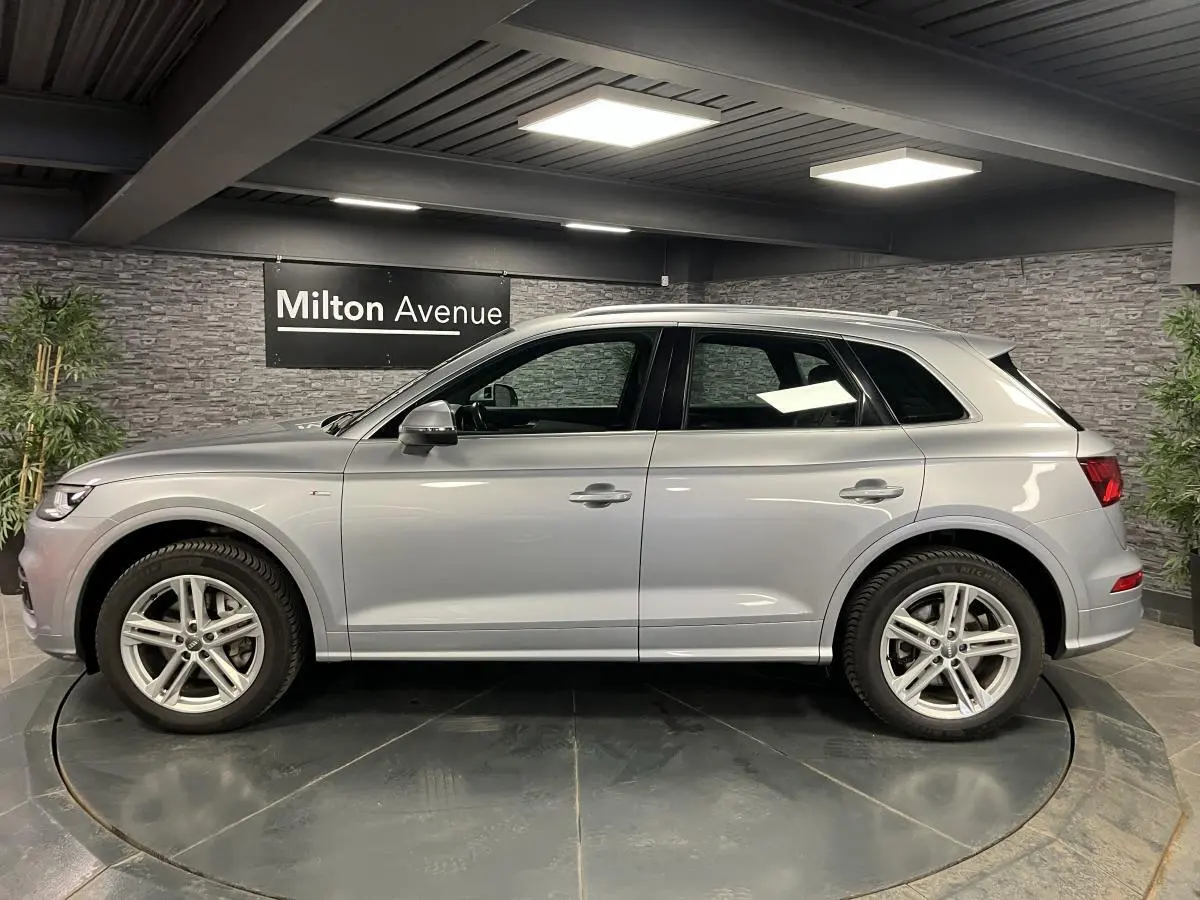 Profil côté gauche d'un Audi Q5 gris métallisé S line 2019 dans un showroom avec jantes 5 branches doubles.