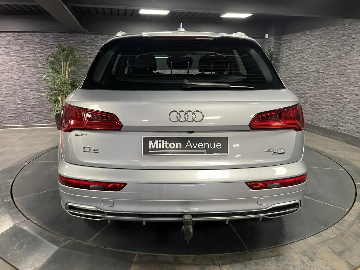 Vue arrière d'un Audi Q5 gris avec hayon électrique et crochet d'attelage rétractable visible en intérieur showroom.