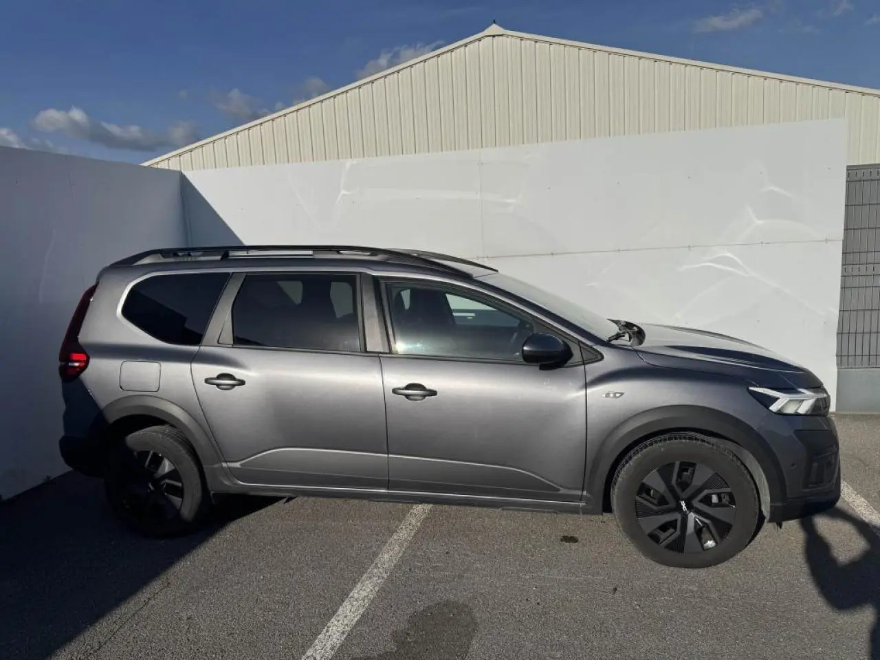 Vue de profil droit d'un Dacia Jogger gris schiste métallisé avec barres de toit et jantes noires.