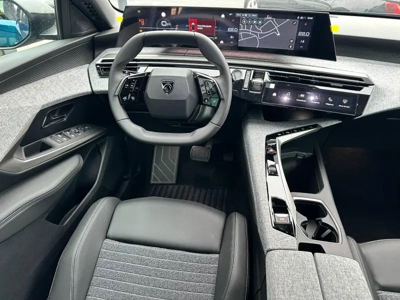 Vue intérieure avant du Peugeot 3008 Hybrid 2025, tableau de bord numérique et volant cuir multifonction gris et noir.