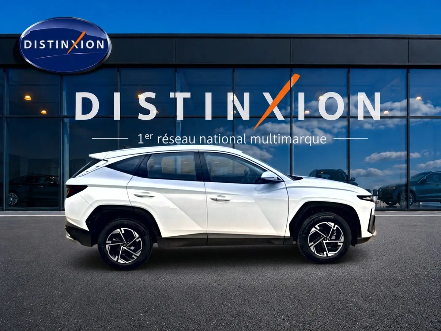 Vue latérale droite d'un Hyundai Tucson blanc 2026 avec jantes alliage 17 pouces devant une vitrine Distinxion.