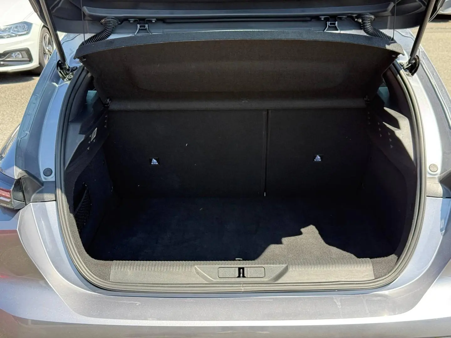Coffre ouvert vu de l'arrière d'une Peugeot 308 e-308 noire, montrant l'espace de chargement vide et l'intérieur sombre.