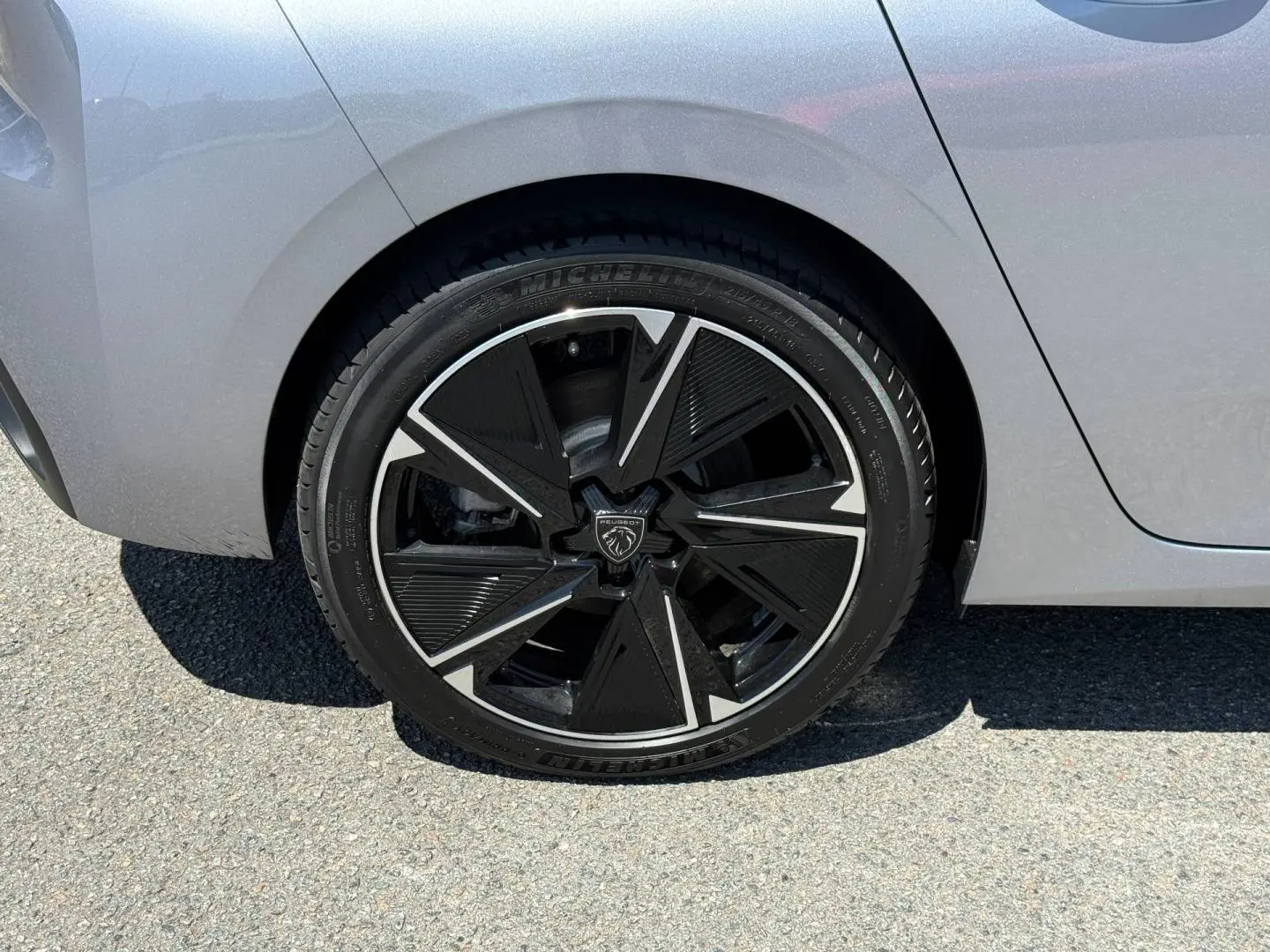 Gros plan sur la roue arrière droite de la Peugeot e-308 2025 gris clair avec jante alu noire et argentée au design géométrique.