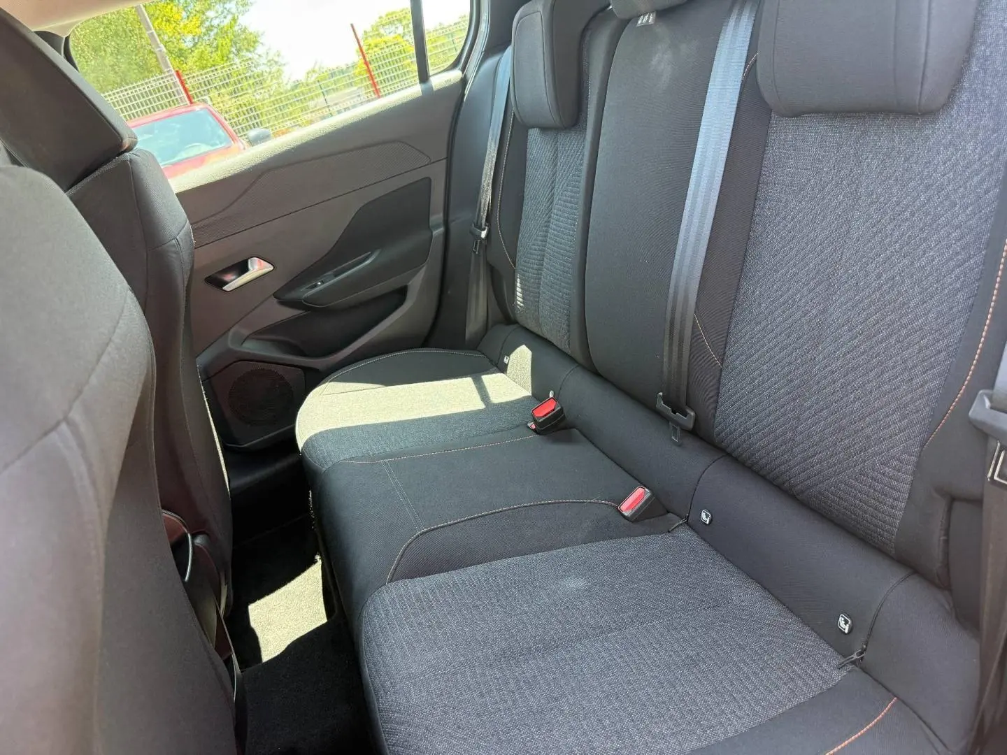 Vue intérieure côté droit montrant la banquette arrière en tissu noir avec surpiqûres orange de la Peugeot 308 e-308 2025.