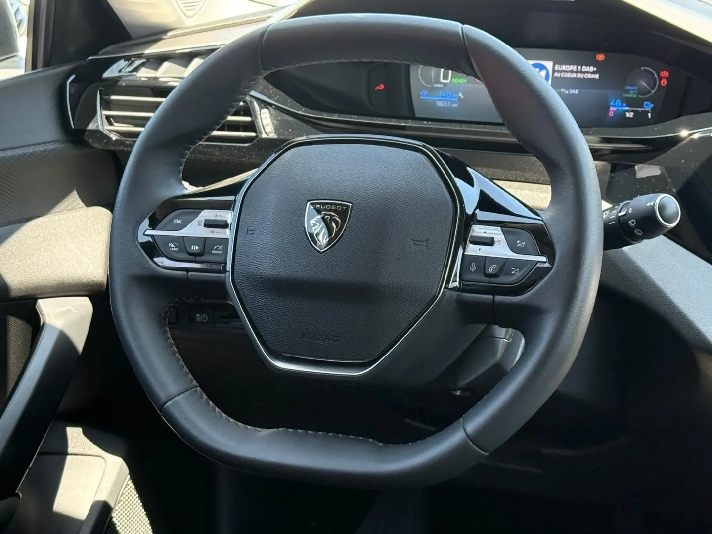 Vue rapprochée du volant multifonction noir de la Peugeot e-308 2025 avec tableau de bord digital en arrière-plan.