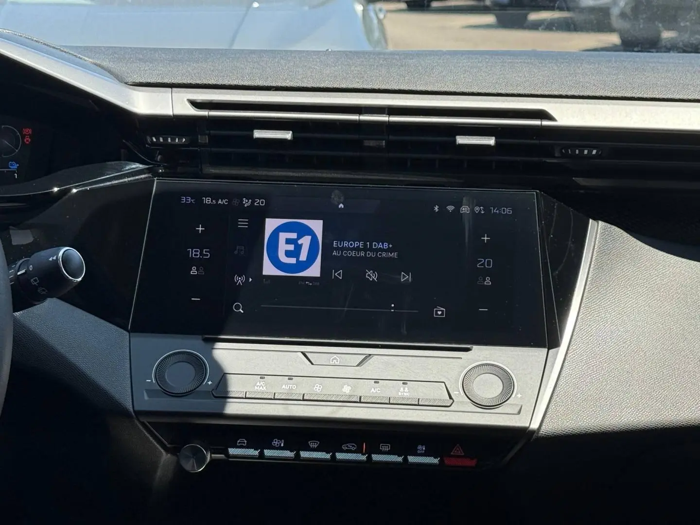 Vue rapprochée de la console centrale tactile noire de la Peugeot e-308 2025 avec commandes climatisation et radio numérique.