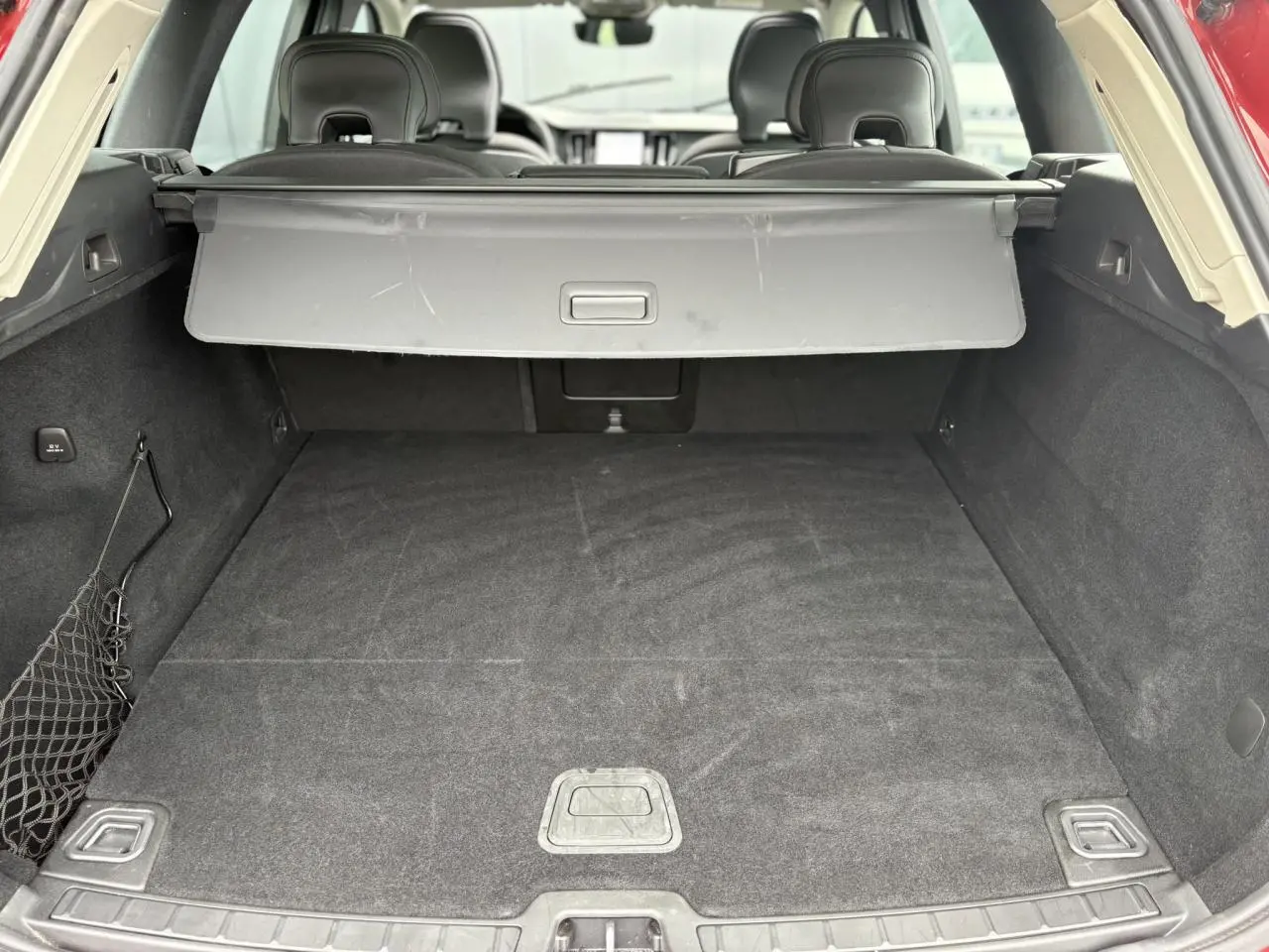 Coffre ouvert du Volvo XC60 rouge Fusion, vue arrière montrant l'espace de chargement avec cache-bagages déployé.