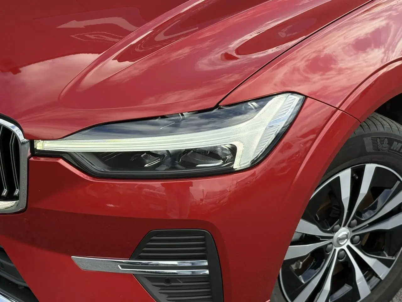 Gros plan sur l'avant droit du Volvo XC60 rouge Fusion, mettant en valeur le phare LED et la jante alliage 18 pouces.