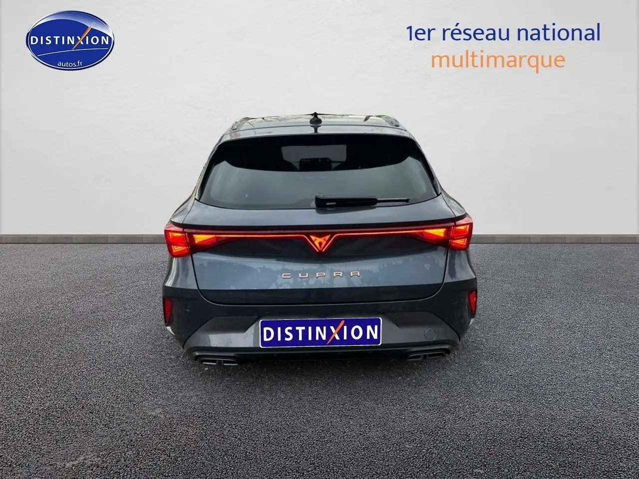 Vue arrière d'une CUPRA Leon ST gris magnétique avec feux arrière LED allumés et double sortie d'échappement.