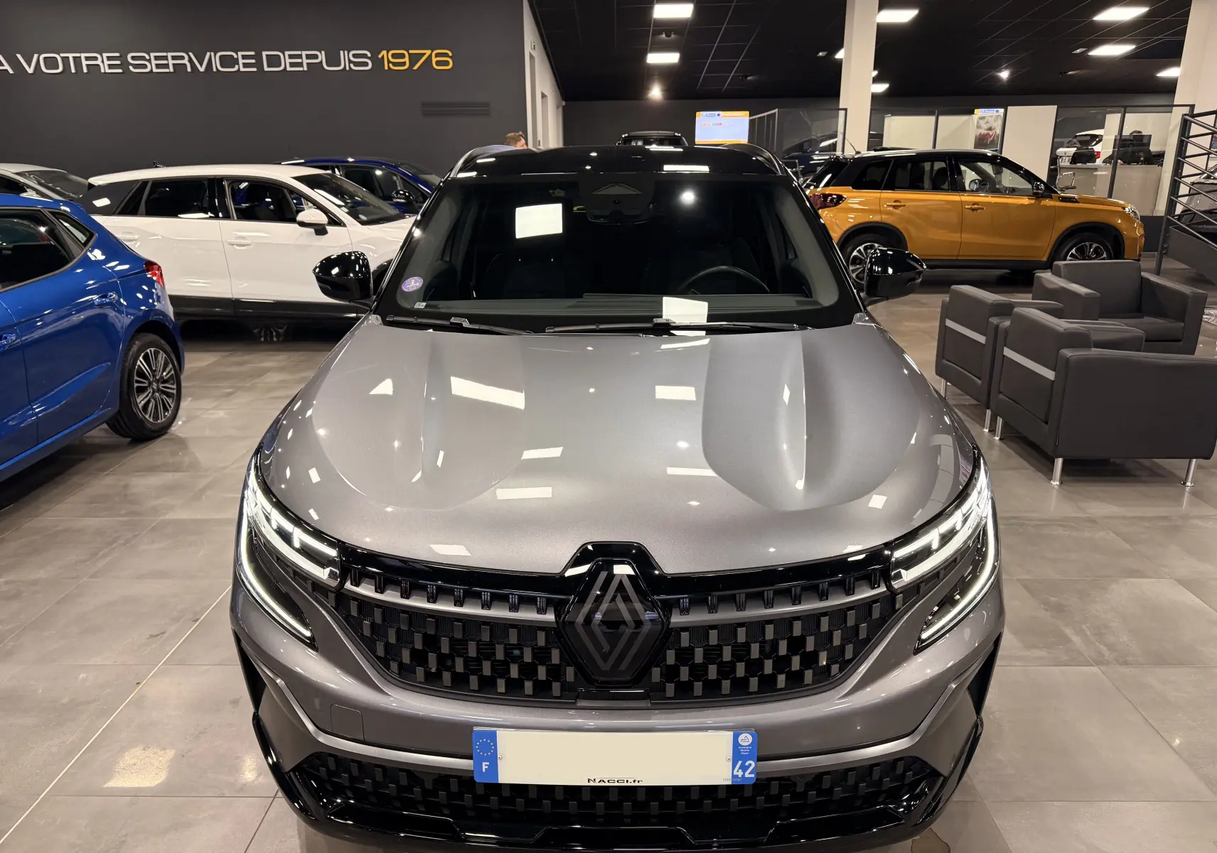 Vue avant d'un Renault Austral E-Tech gris schist avec toit noir, mettant en valeur sa calandre et ses phares LED en showroom.