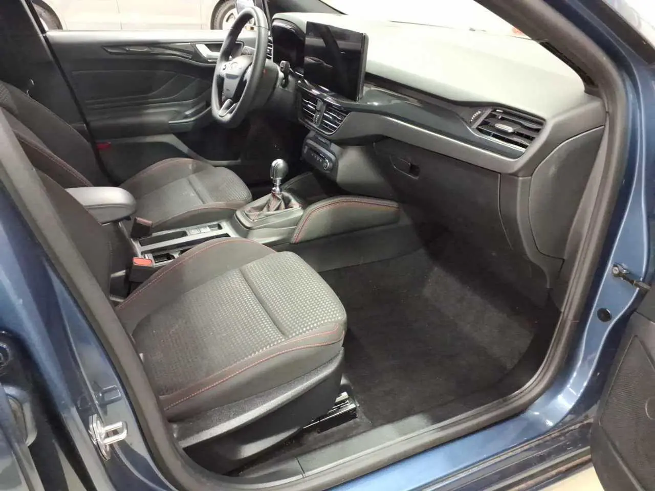 Intérieur côté conducteur d'une Ford Focus SW Bleu Azur 2023, avec sièges noirs surpiqûres rouges et tableau de bord moderne.