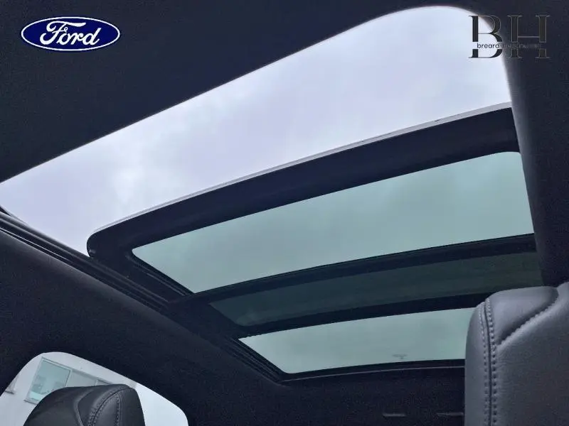 Toit ouvrant panoramique ouvert vu de l'intérieur sur un DS7 gris laqué avec ciel nuageux visible.