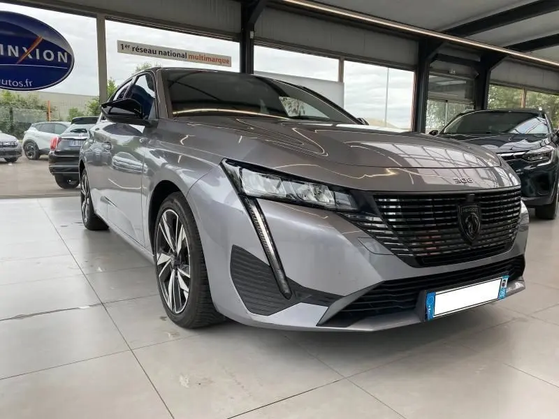 Peugeot 308 2022 gris Artense vue 3/4 avant droit dans un showroom avec calandre noire distinctive.