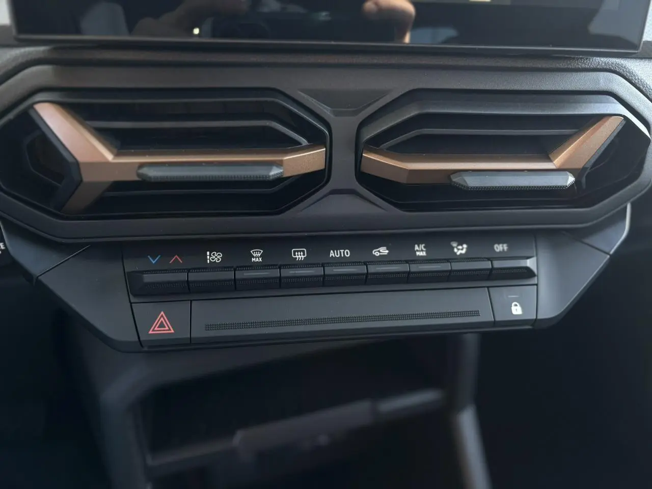 Détail du tableau de bord du Dacia Duster 2026, avec aérateurs brun cuivré et commandes de climatisation noires.