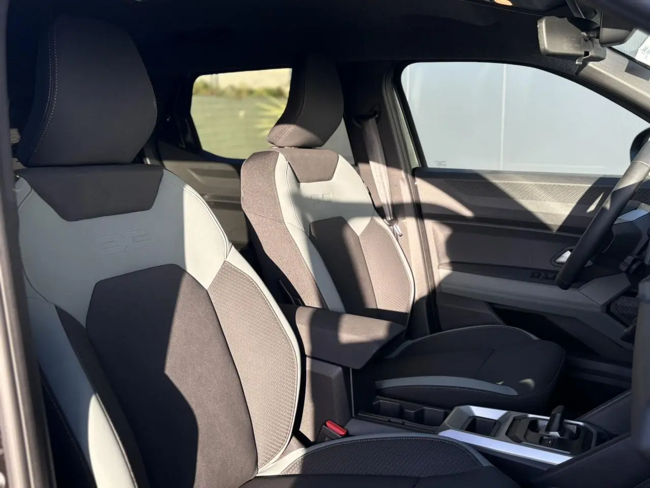 Vue intérieure côté conducteur du Dacia Duster 2026 avec sièges bi-matière gris et noir et console centrale moderne.