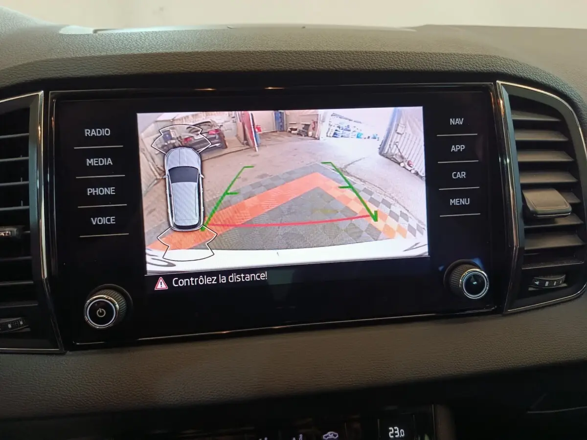 Écran tactile central montrant la caméra de recul avec vue aérienne du Skoda Karoq blanc en stationnement.