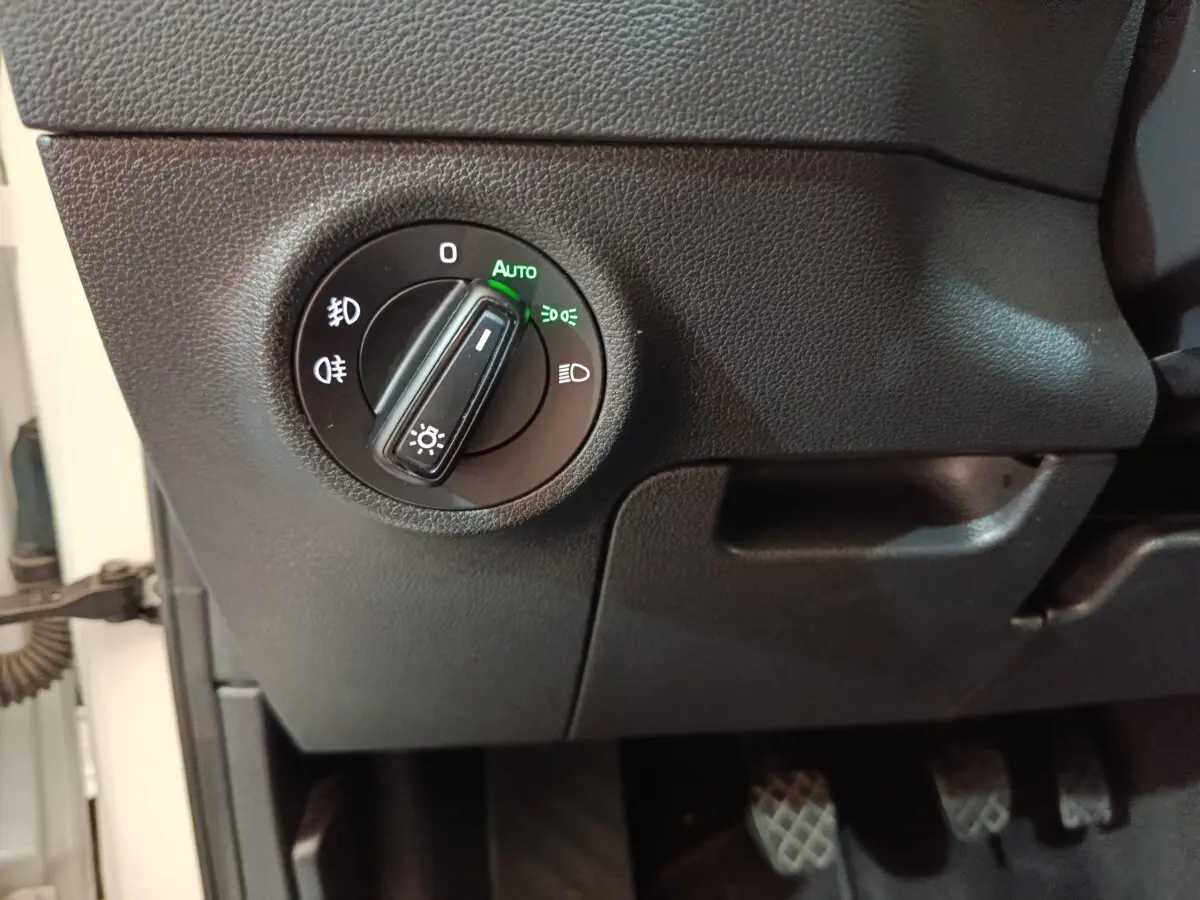 Gros plan sur la commande des phares à gauche du volant dans l'habitacle noir du Skoda Karoq blanc 2024.