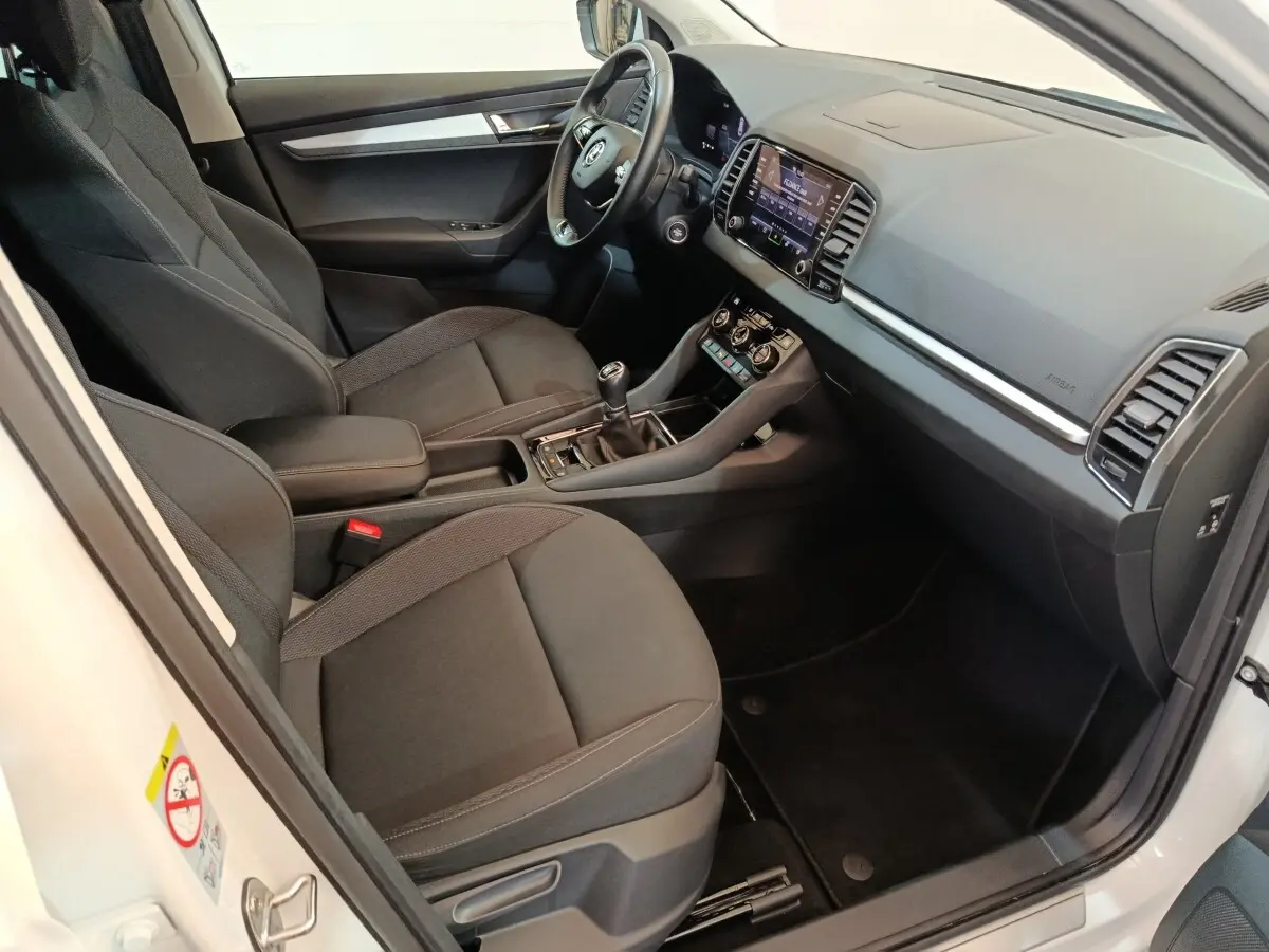 Intérieur avant droit du Skoda Karoq blanc 2024, sièges noirs, tableau de bord avec écran tactile et volant multifonctions cuir.
