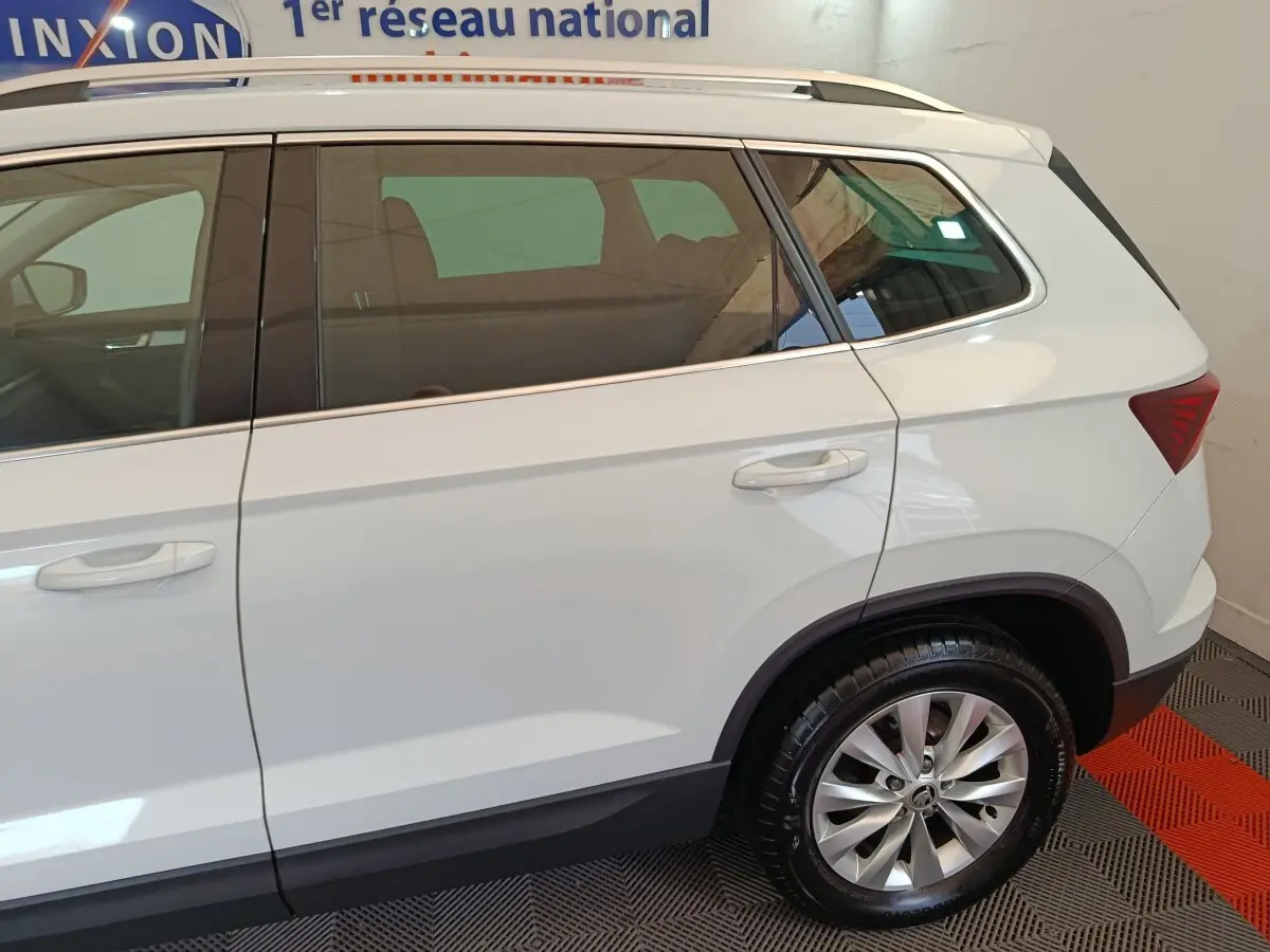 Vue latérale côté droit d'un SKODA KAROQ blanc, mettant en valeur la porte arrière et la roue arrière sur sol intérieur.