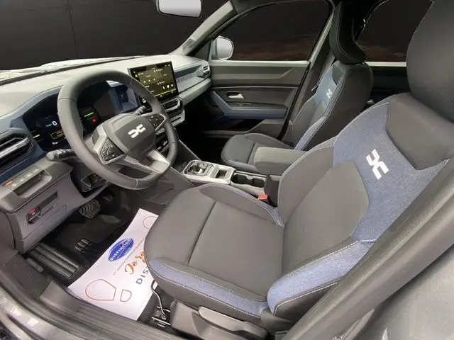 Vue intérieure côté conducteur du Dacia Duster 1.6 Hybrid 140 gris schiste, avec sièges tissu bi-ton et tableau de bord moderne.