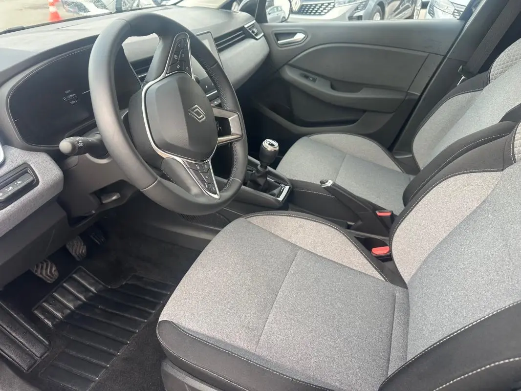Vue intérieure côté conducteur de la Renault Clio V dCi 100 Evolution 2025, montrant le volant, la boîte manuelle et les sièges gris.
