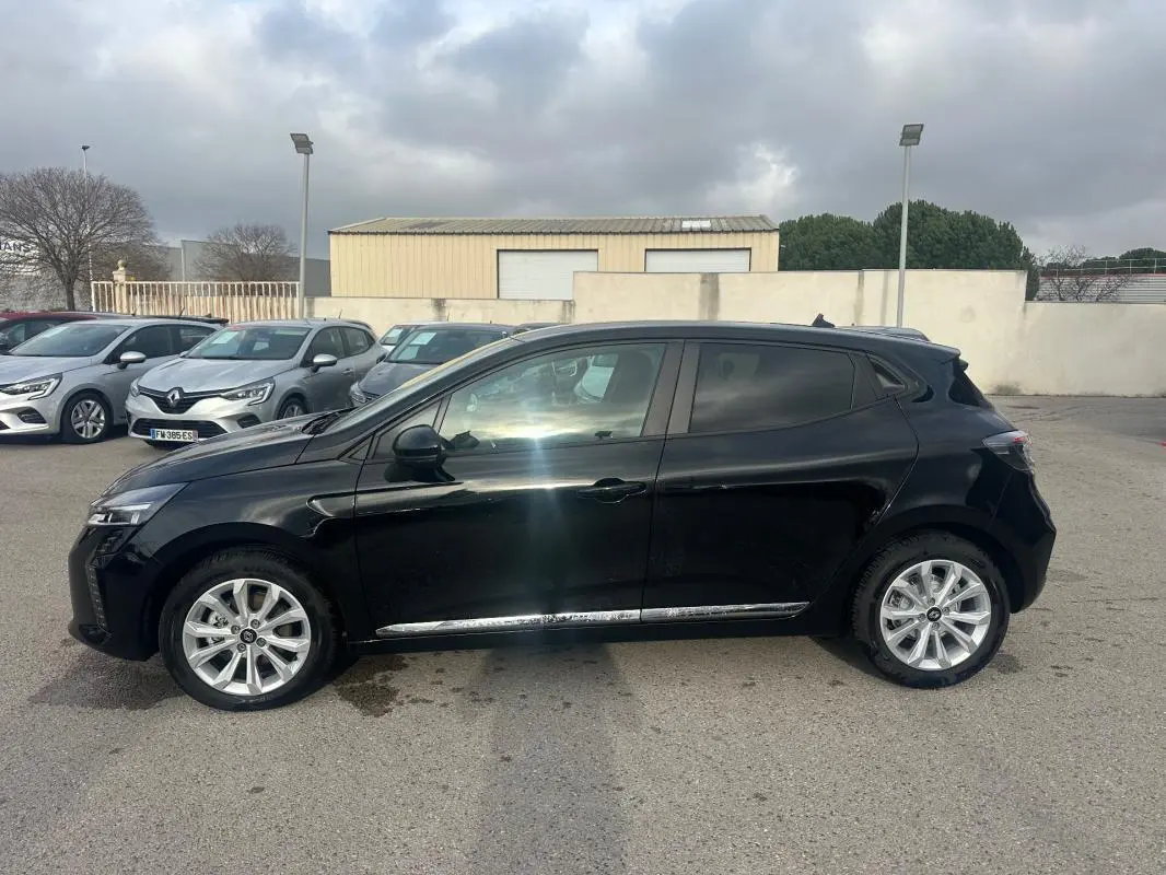 Profil côté gauche d'une Renault Clio V dCi 100 Evolution noire avec vitres surteintées et jantes argentées, sur parking extérieur.