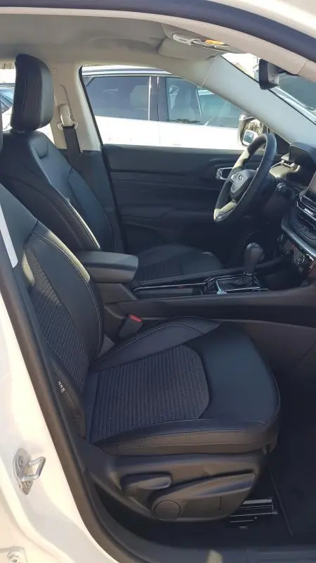 Intérieur du Jeep Compass 2024 blanc vu côté conducteur, sièges noirs avec accoudoir central et tableau de bord moderne.
