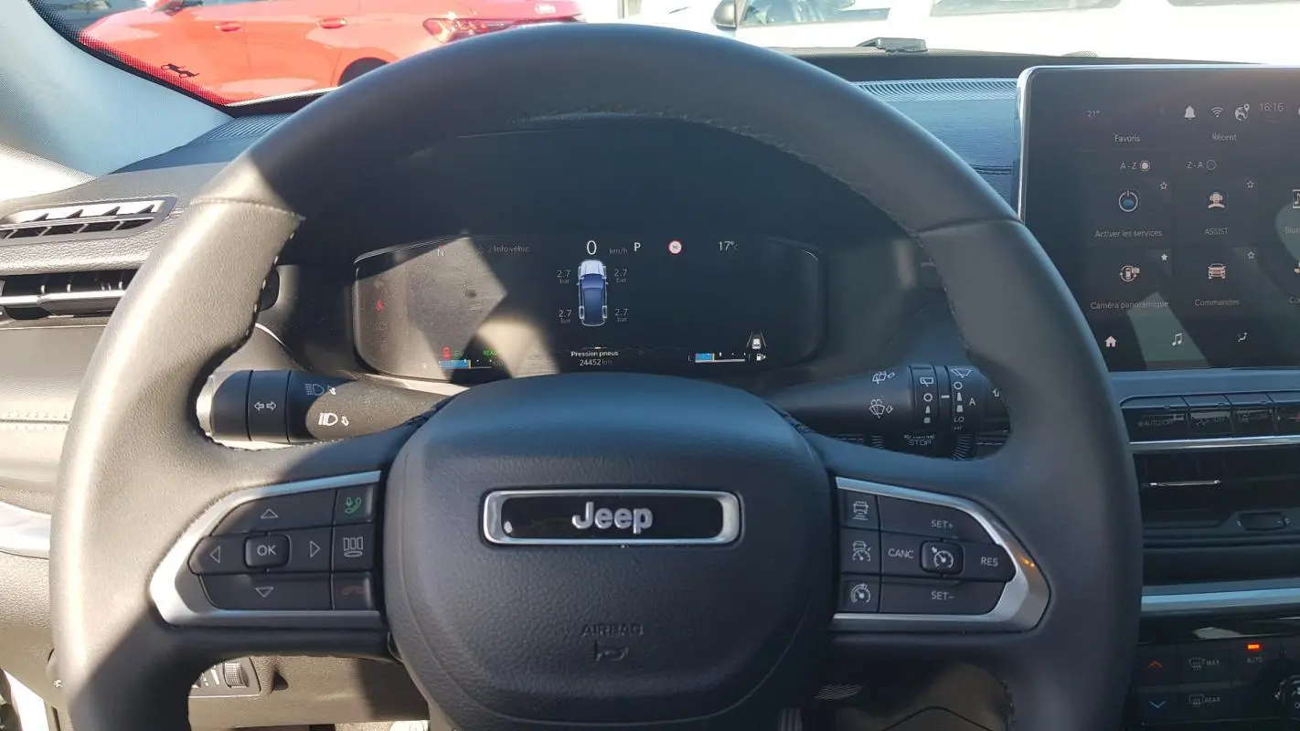 Vue rapprochée du volant Jeep Compass 2024 avec commandes intégrées et tableau de bord numérique allumé.