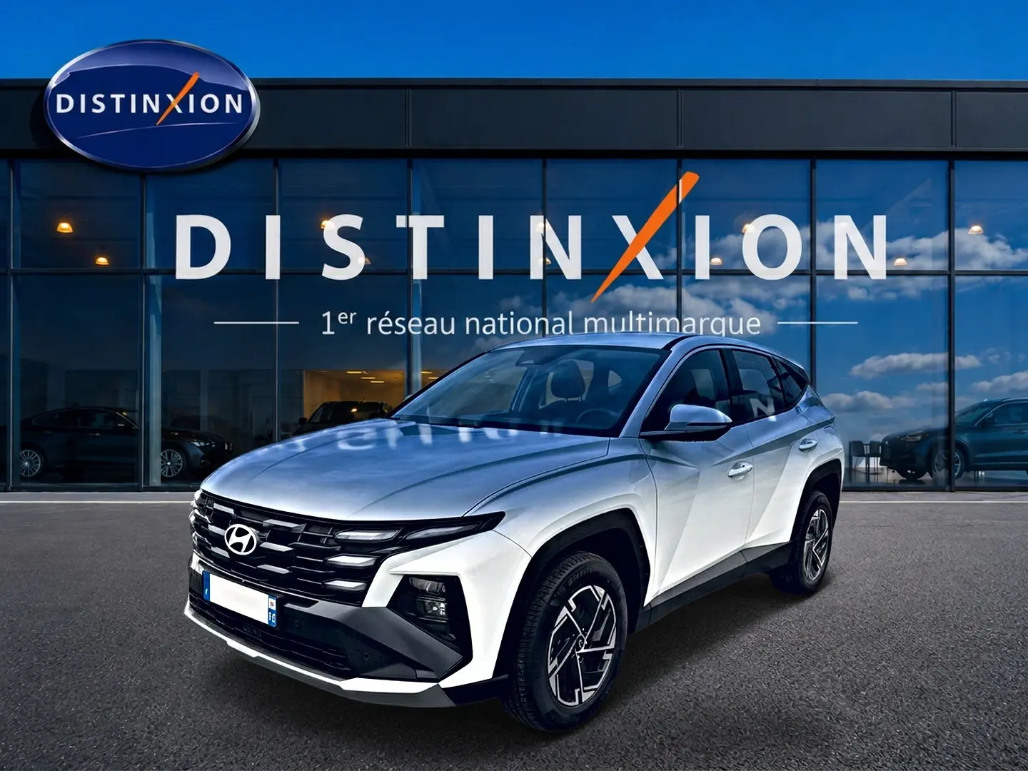 Hyundai Tucson blanc en 3/4 avant droit, avec calandre noire et jantes alliage distinctives devant showroom Distinxion.
