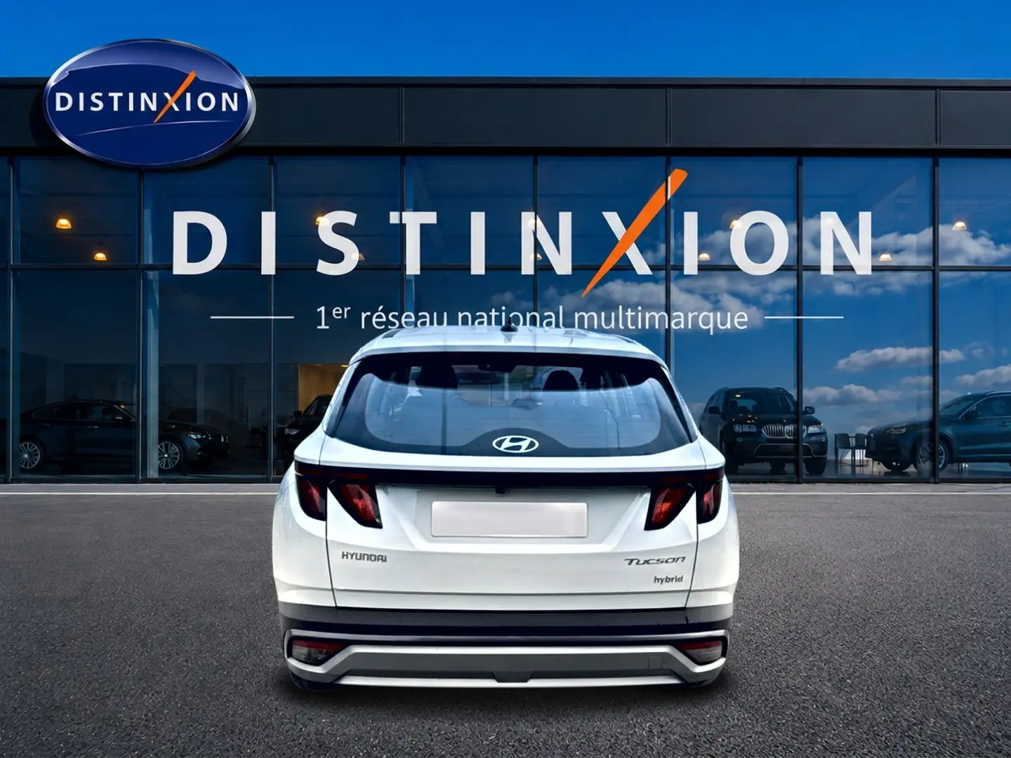 Vue arrière d'un Hyundai Tucson blanc hybride 2026 stationné devant une vitrine avec logo Distinxion.