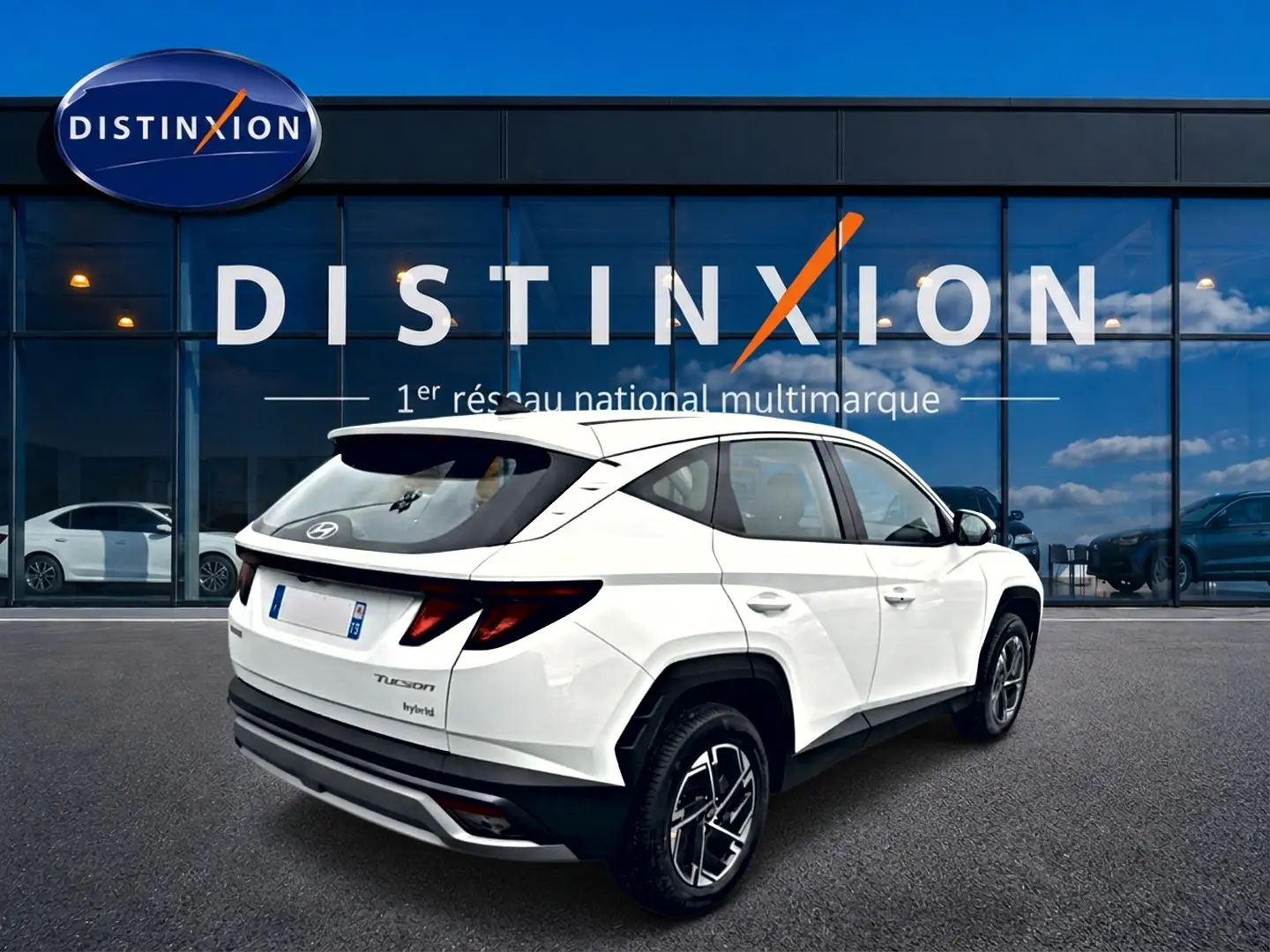 Vue 3/4 arrière droite d'un Hyundai Tucson blanc hybride devant une vitrine avec logo Distinxion.