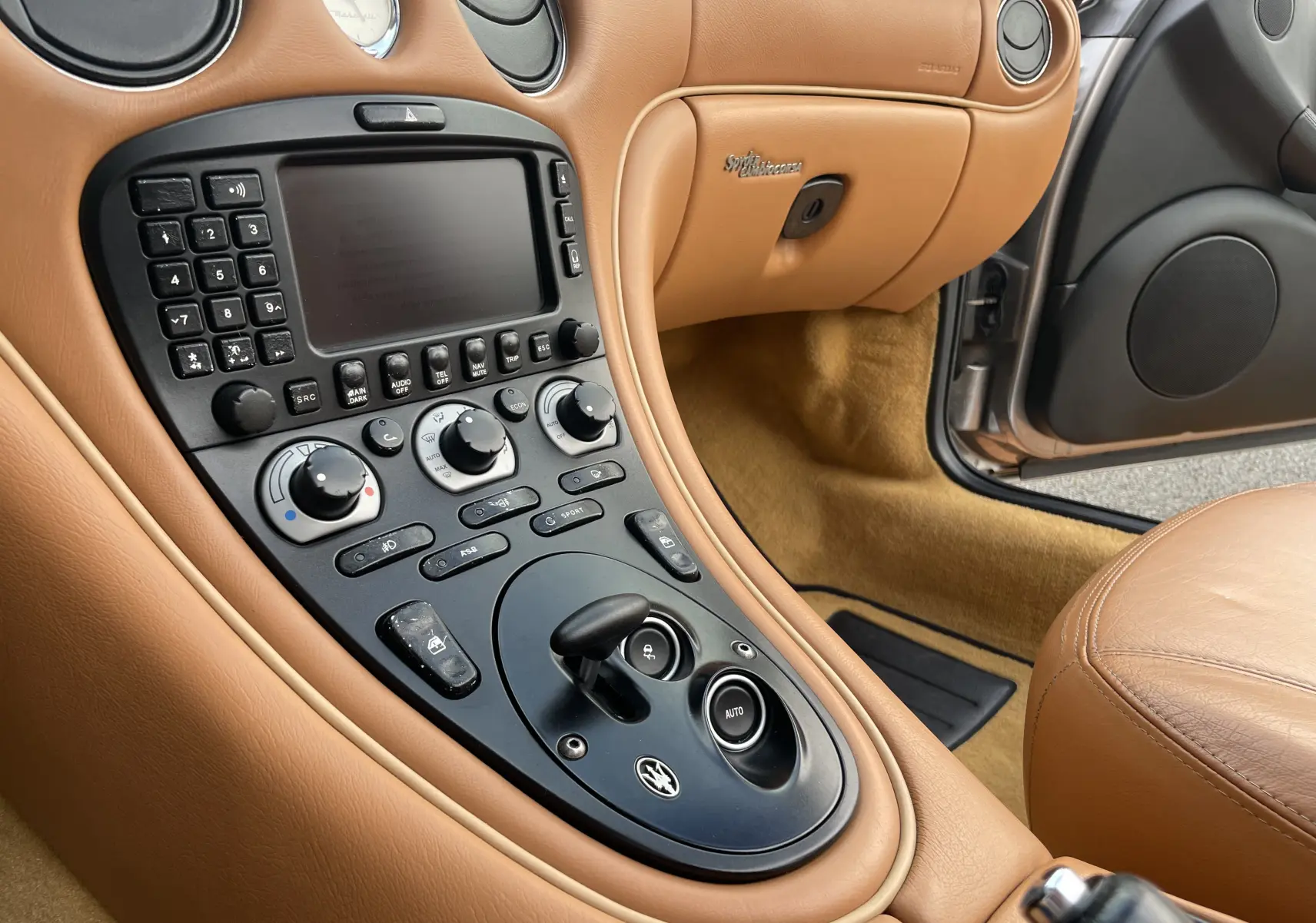 Vue rapprochée de la console centrale en cuir beige de la Maserati Spyder 2002 avec commandes et levier de boîte automatique.