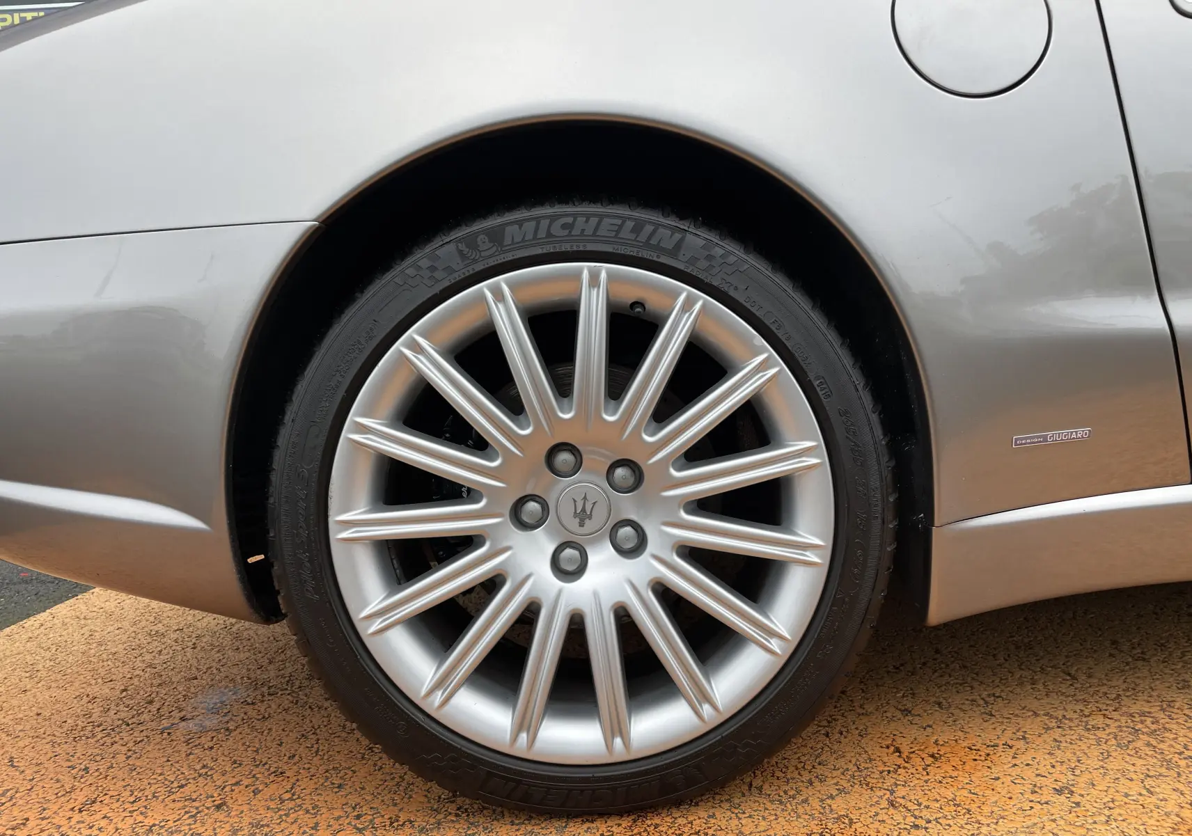 Gros plan sur la roue arrière droite gris Nuvolari d'une Maserati Spyder 2002 avec jante étoilée et badge Giugiaro.