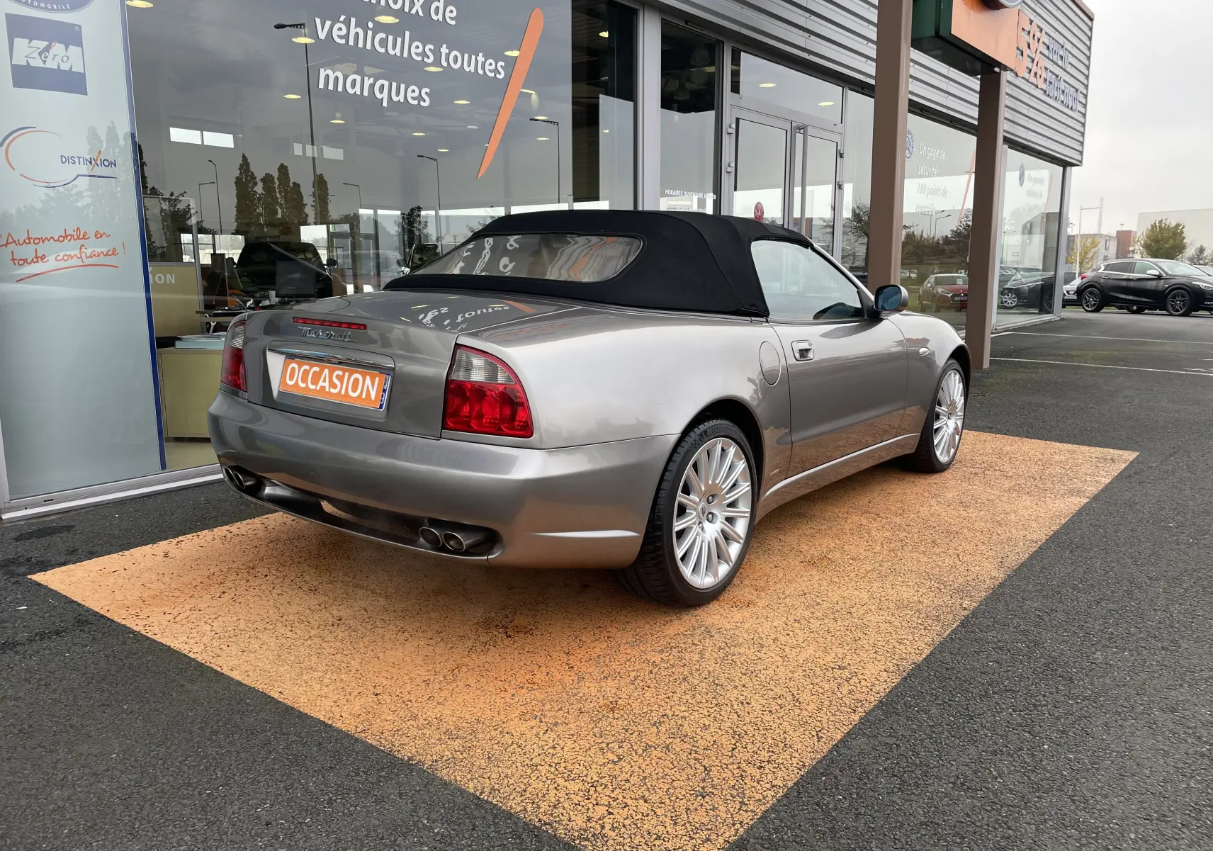 Maserati Spyder gris Nuvolari vue 3/4 arrière droit, capote noire fermée, jantes alliage et double sortie d'échappement.