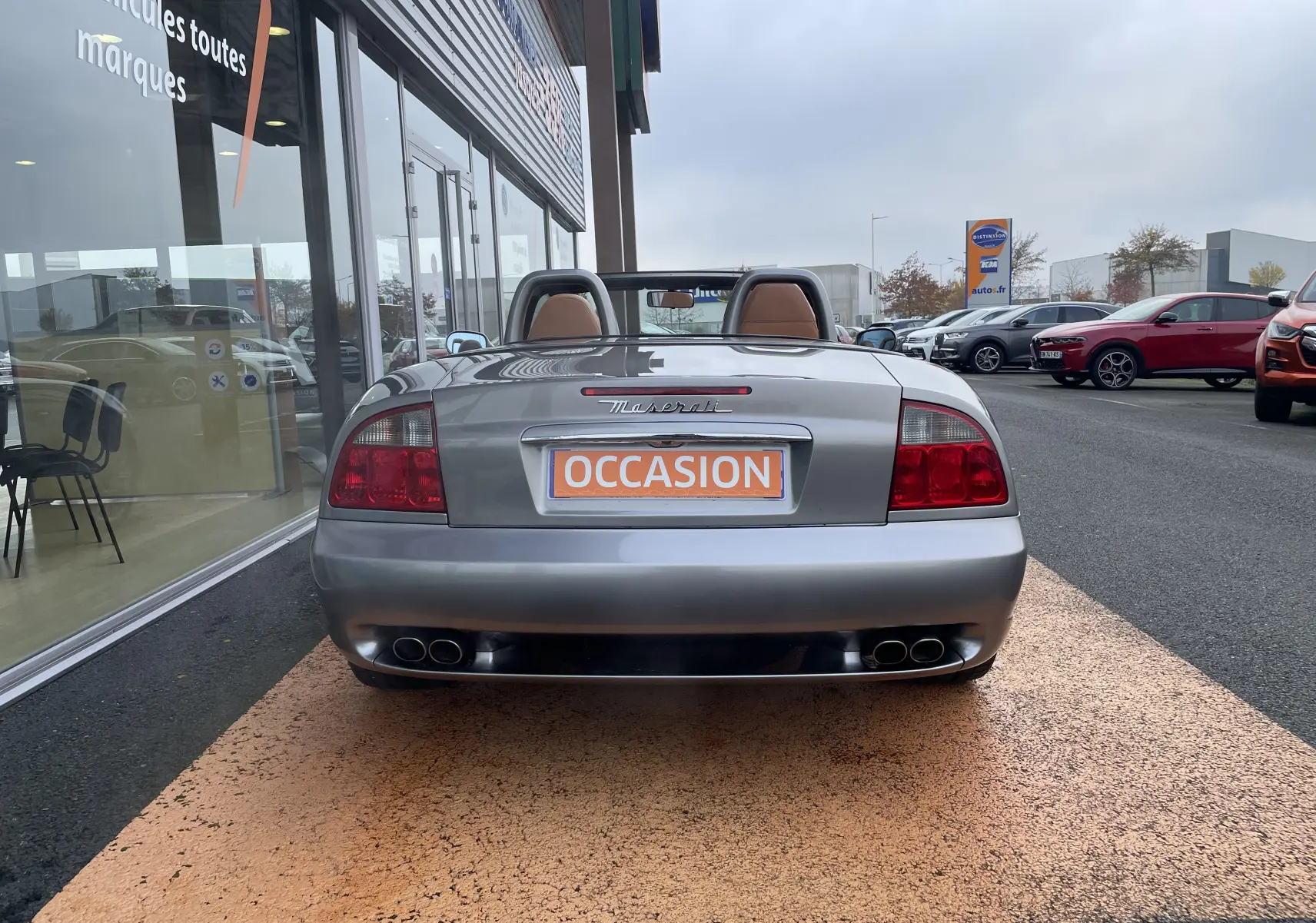 Vue arrière d'une Maserati Spyder gris Nuvolari de 2002 avec capote ouverte et doubles sorties d'échappement chromées.