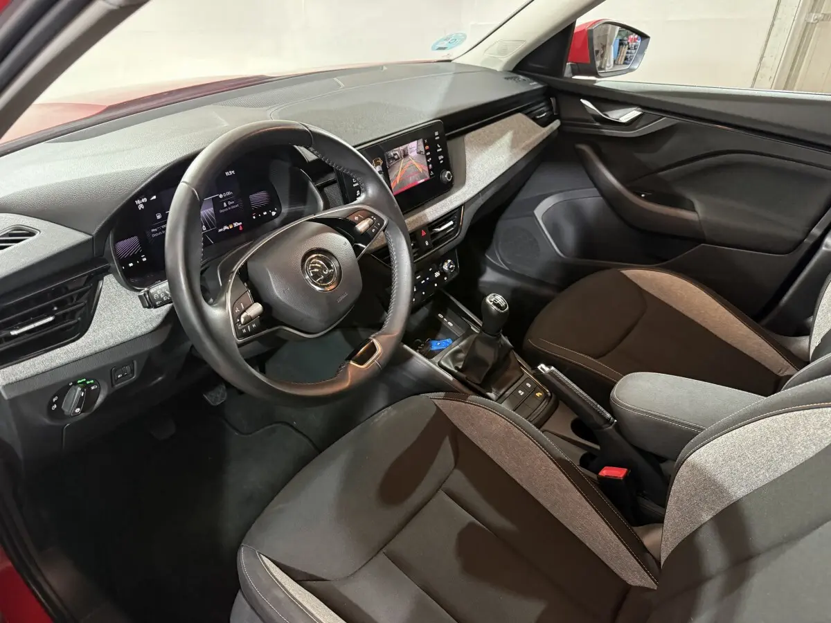 Intérieur de la Skoda Kamiq rouge 2024 vu côté conducteur, avec volant cuir et écran tactile central.
