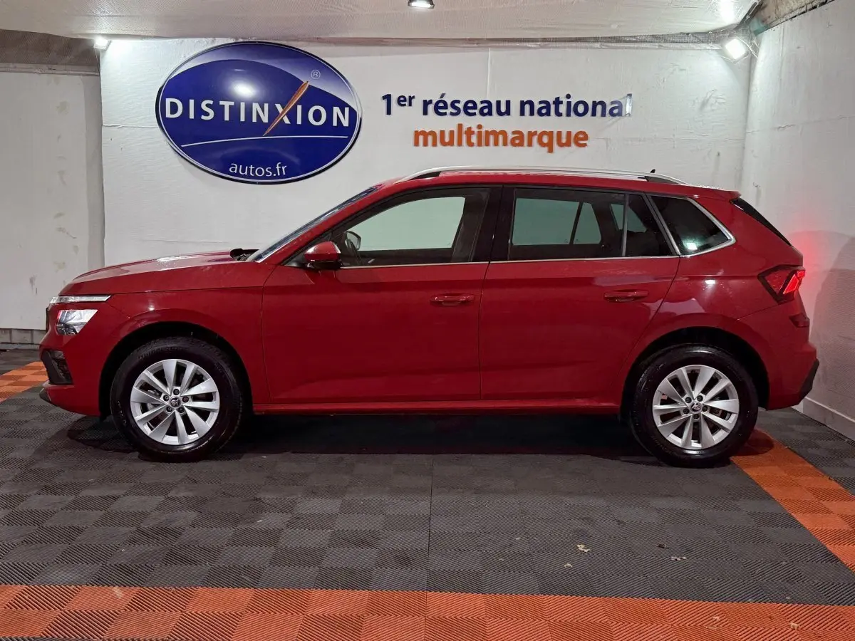 Profil latéral droit d'un SUV SKODA KAMIQ rouge 2024 dans un garage avec sol noir et orange.