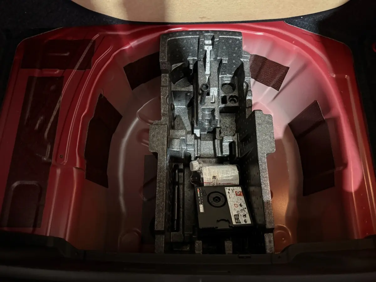 Coffre ouvert du Skoda Kamiq rouge 2024, montrant le rangement sous tablette avec kit de réparation pneus.